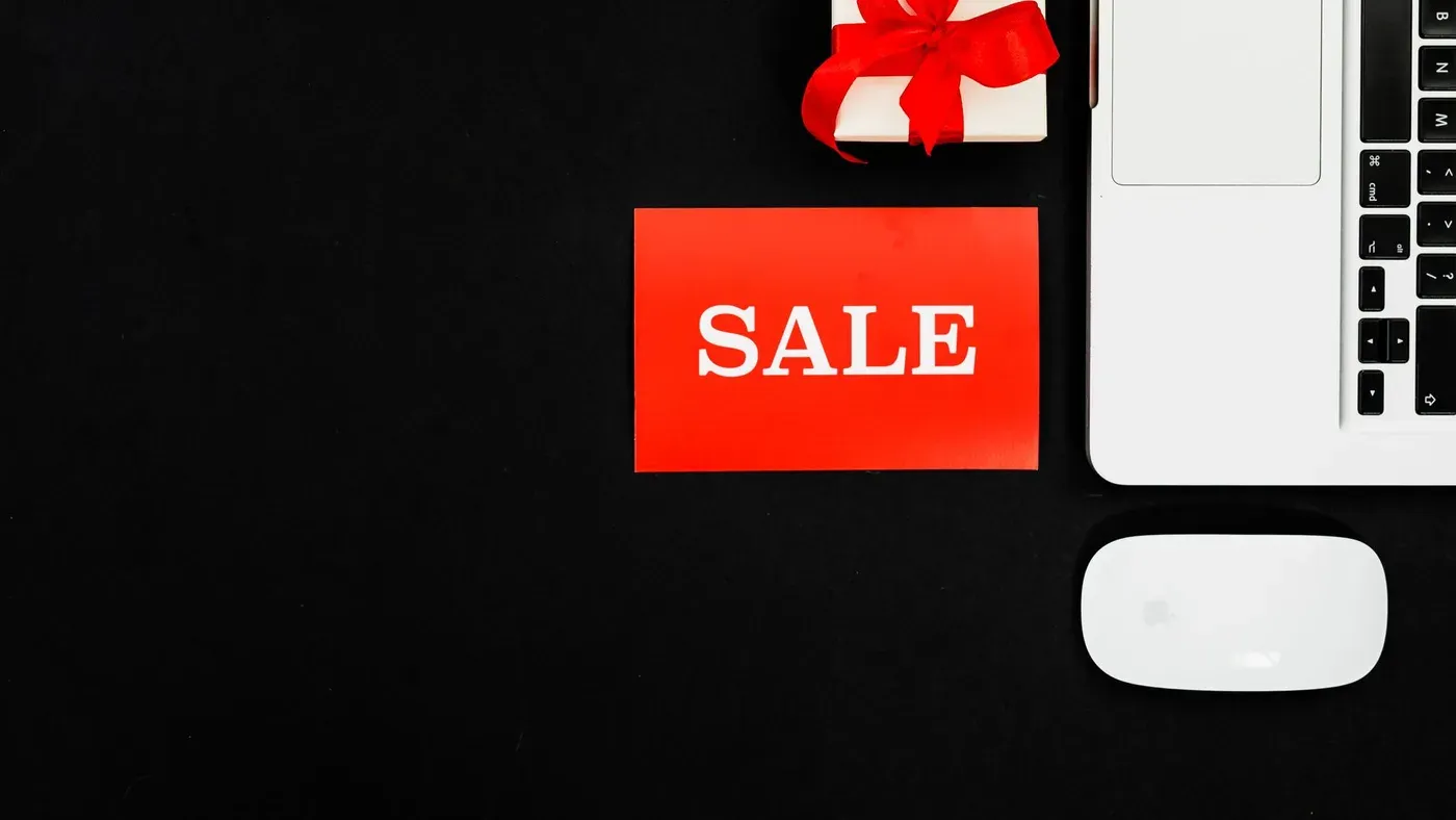 Röd skylt med ordet SALE bredvid en bärbar dator och ett presentpaket på svart bakgrund