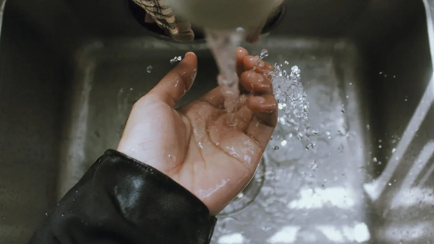 Hand under rinnande vatten från en kran över ett diskho