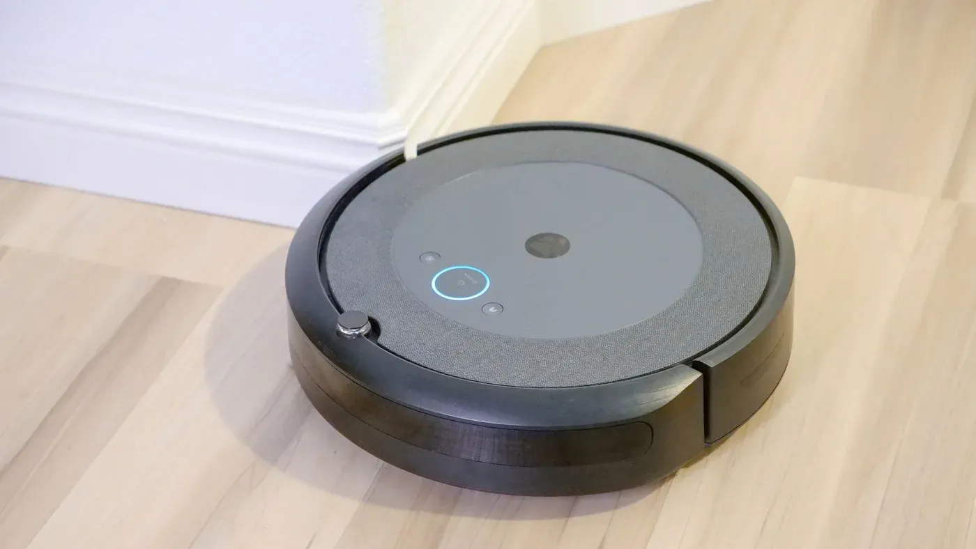 Svart robotdammsugare på ett ljust trägolv intill en vit list