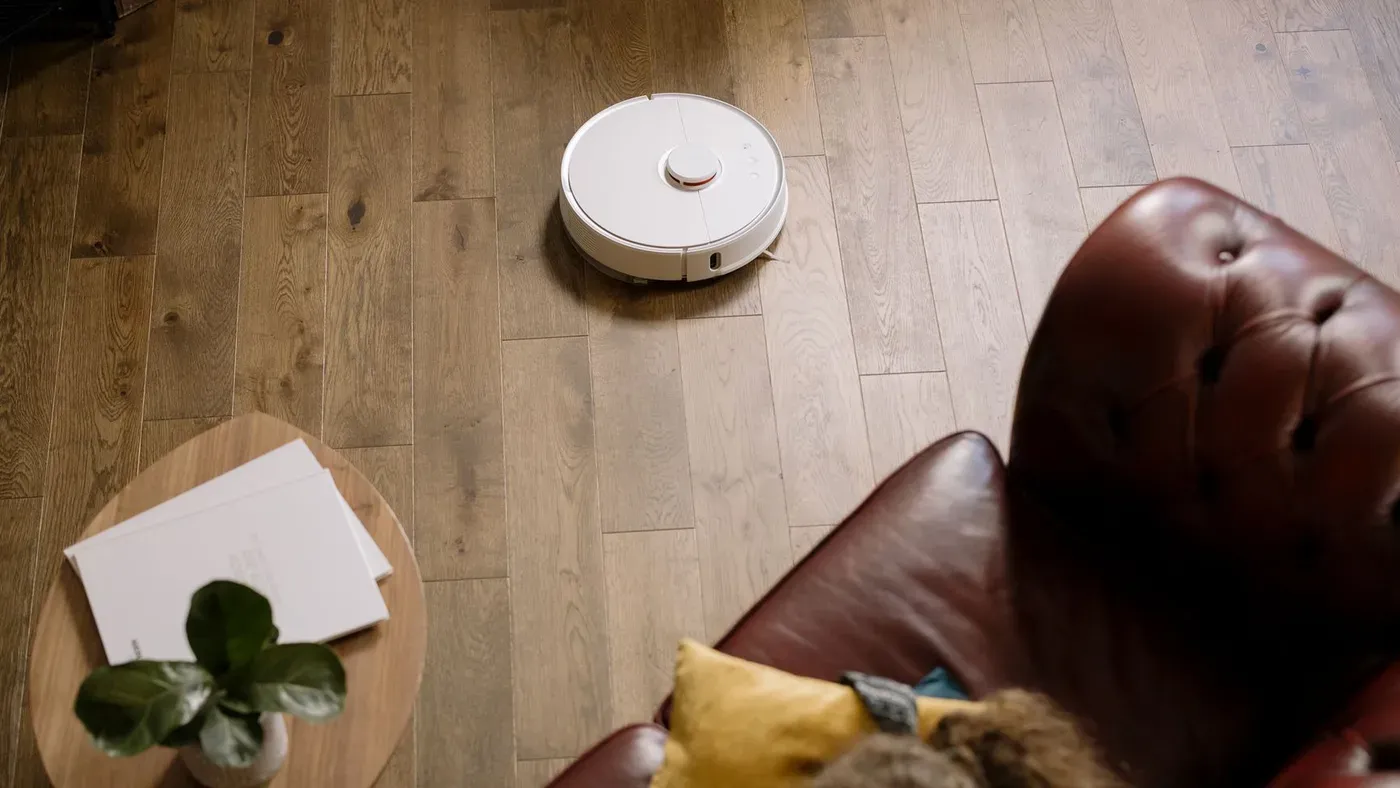 Vit robotdammsugare som kör över ett parkettgolv i ett vardagsrum