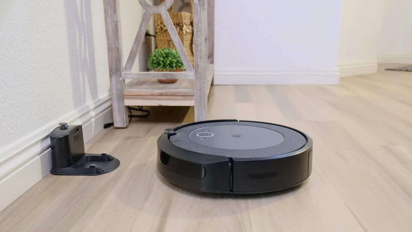 Svart robotdammsugare på ett ljust trägolv bredvid en liten laddningsbas