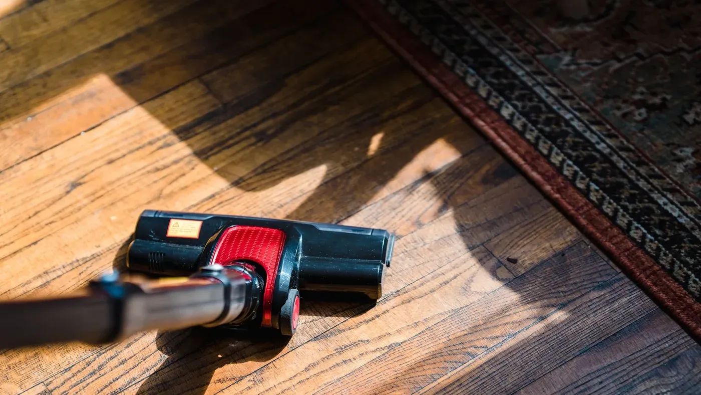 Dammsugarmunstycke med röd detalj på ett trägolv intill kanten av en mönstrad matta