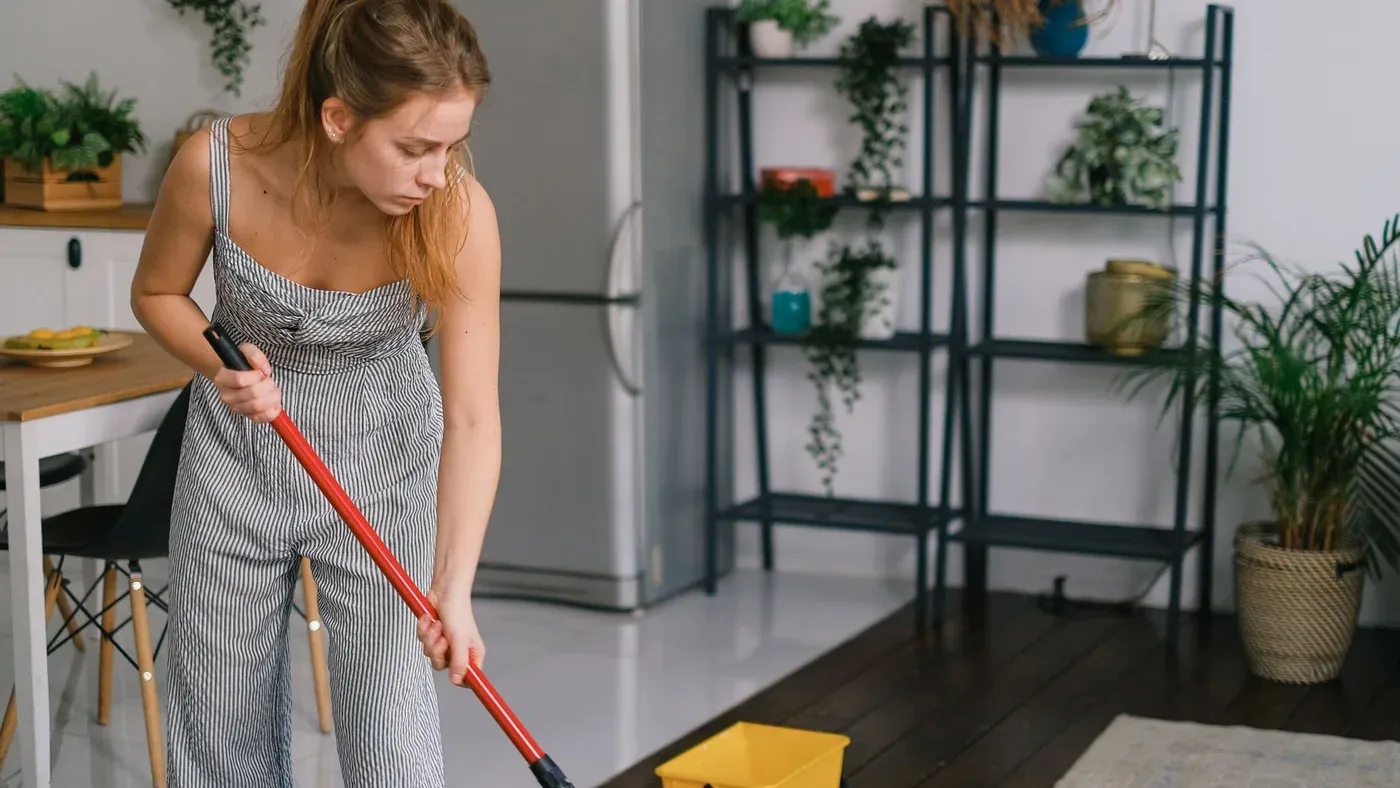 Kvinna i randig overall moppar ett kök med en gul hink stående på golvet