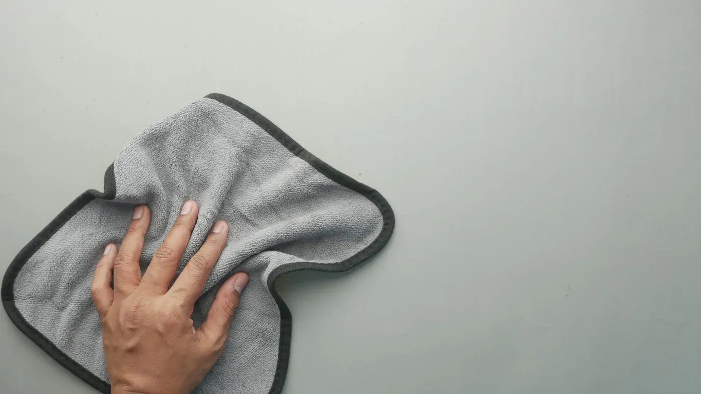 Hand som torkar en grå yta med en microfiberduk