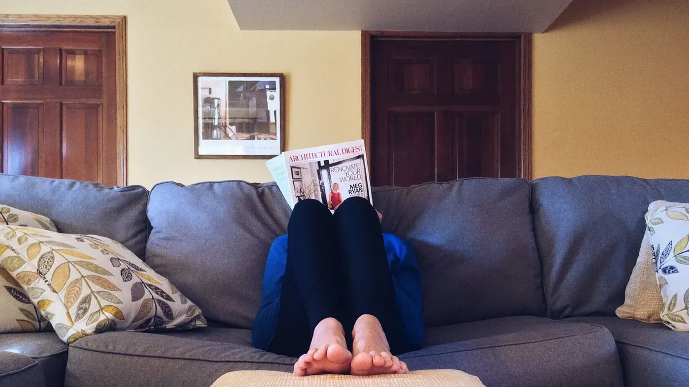 Person som läser en tidning i en blå soffa med fötterna uppe