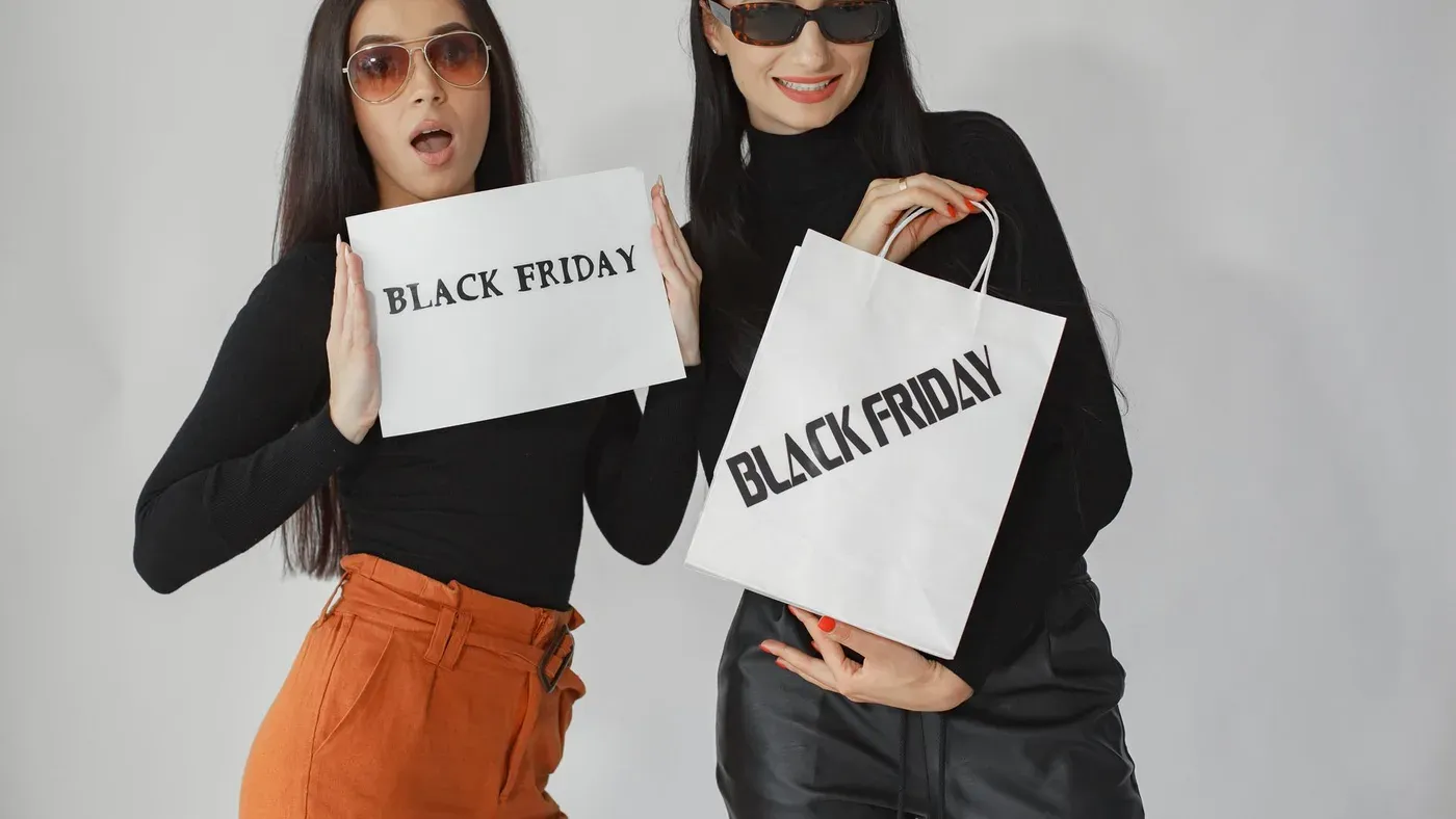 Två kvinnor håller upp en skylt och en kasse med texten Black Friday