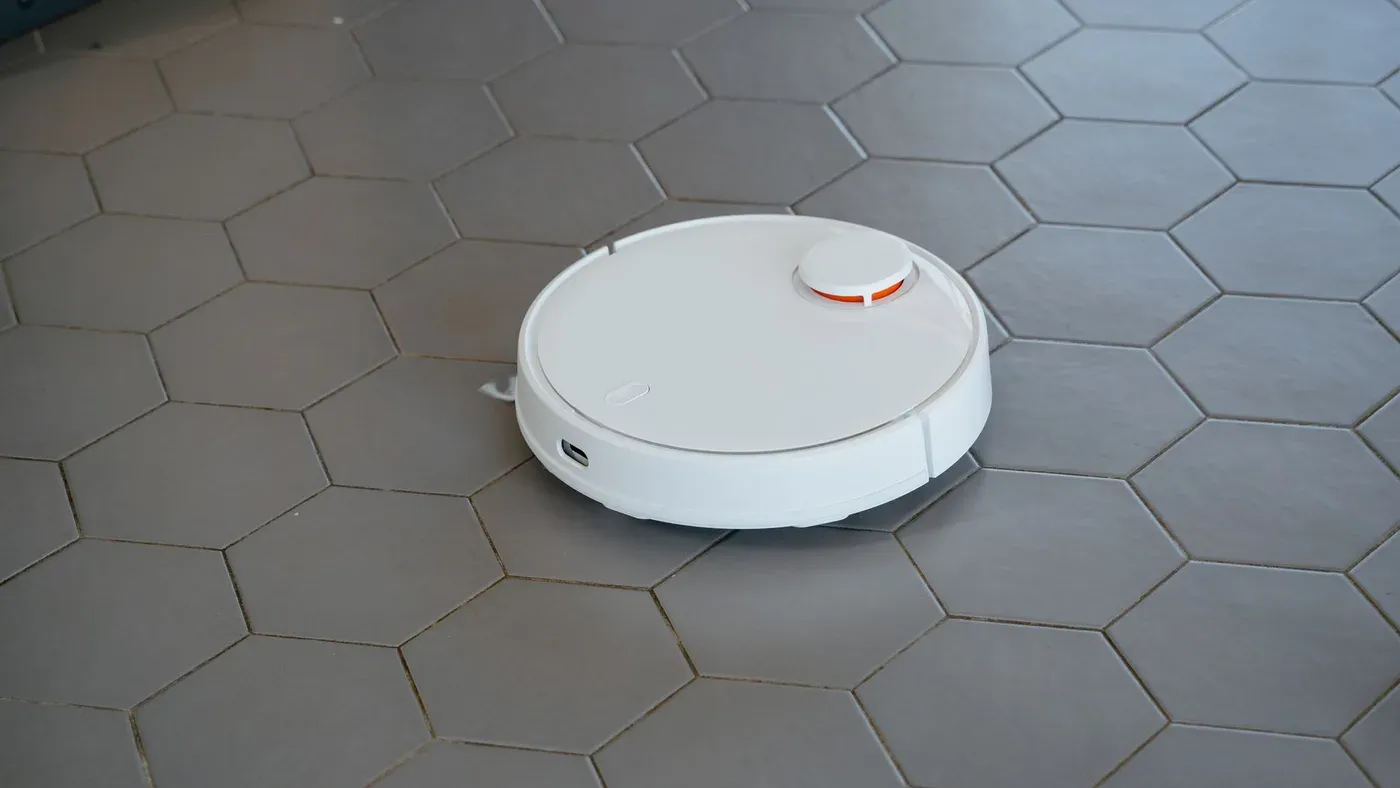 Vit robotdammsugare på ett grått golv med sexkantiga kakelplattor